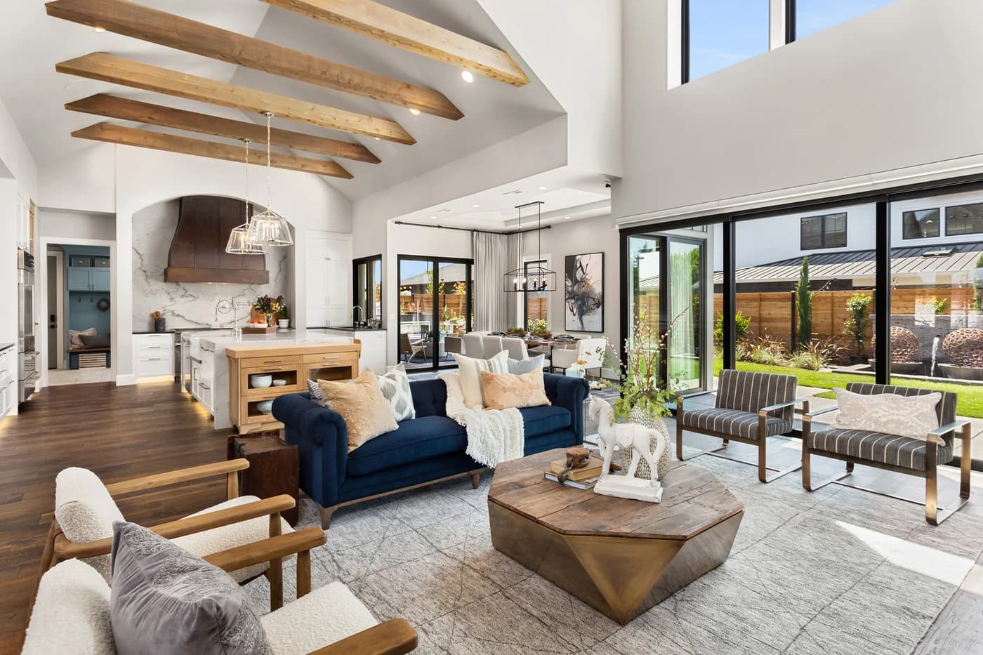 Interior design by Greylyn Wayne in Portland — open-concept living room with vaulted wood-beam ceiling, navy velvet sofas, and a gourmet kitchen from a NW Natural Street of Dreams home